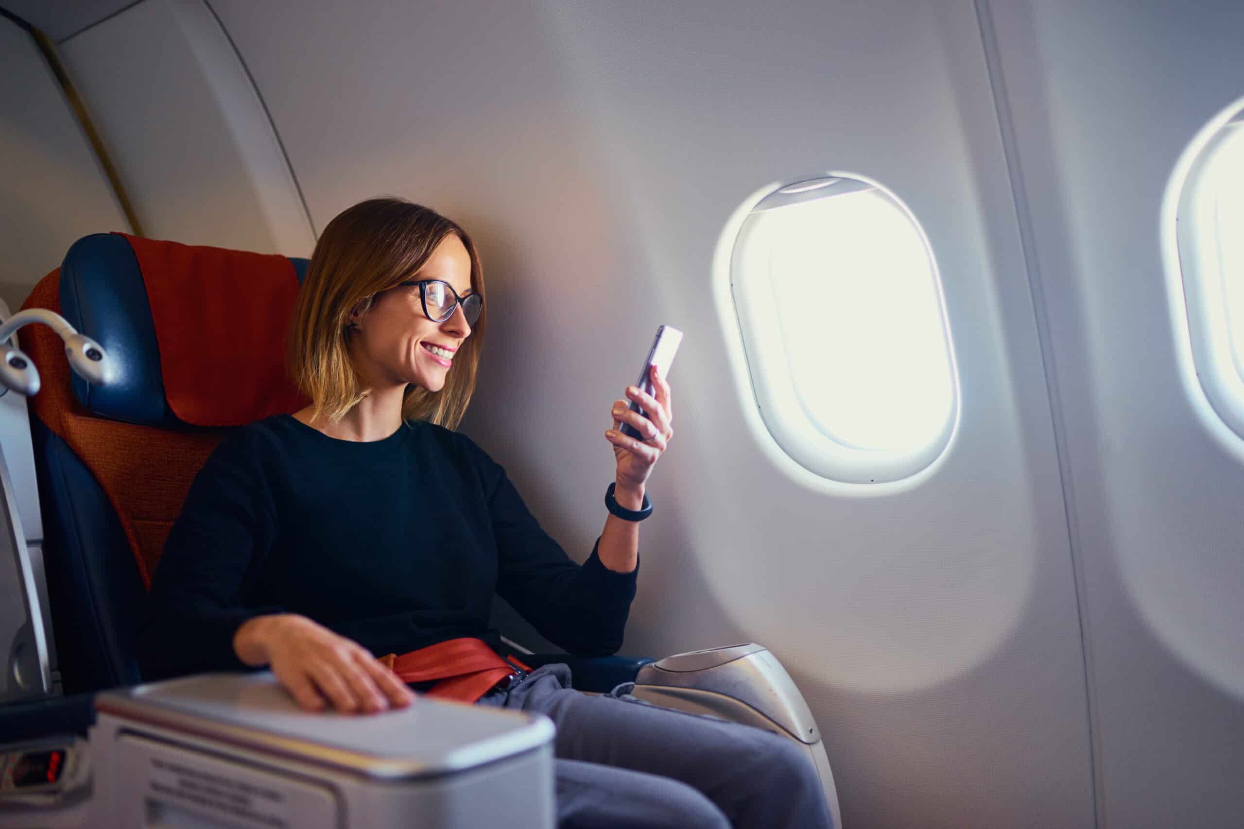 Young woman in a plane checking her travel documents on a mobile phone