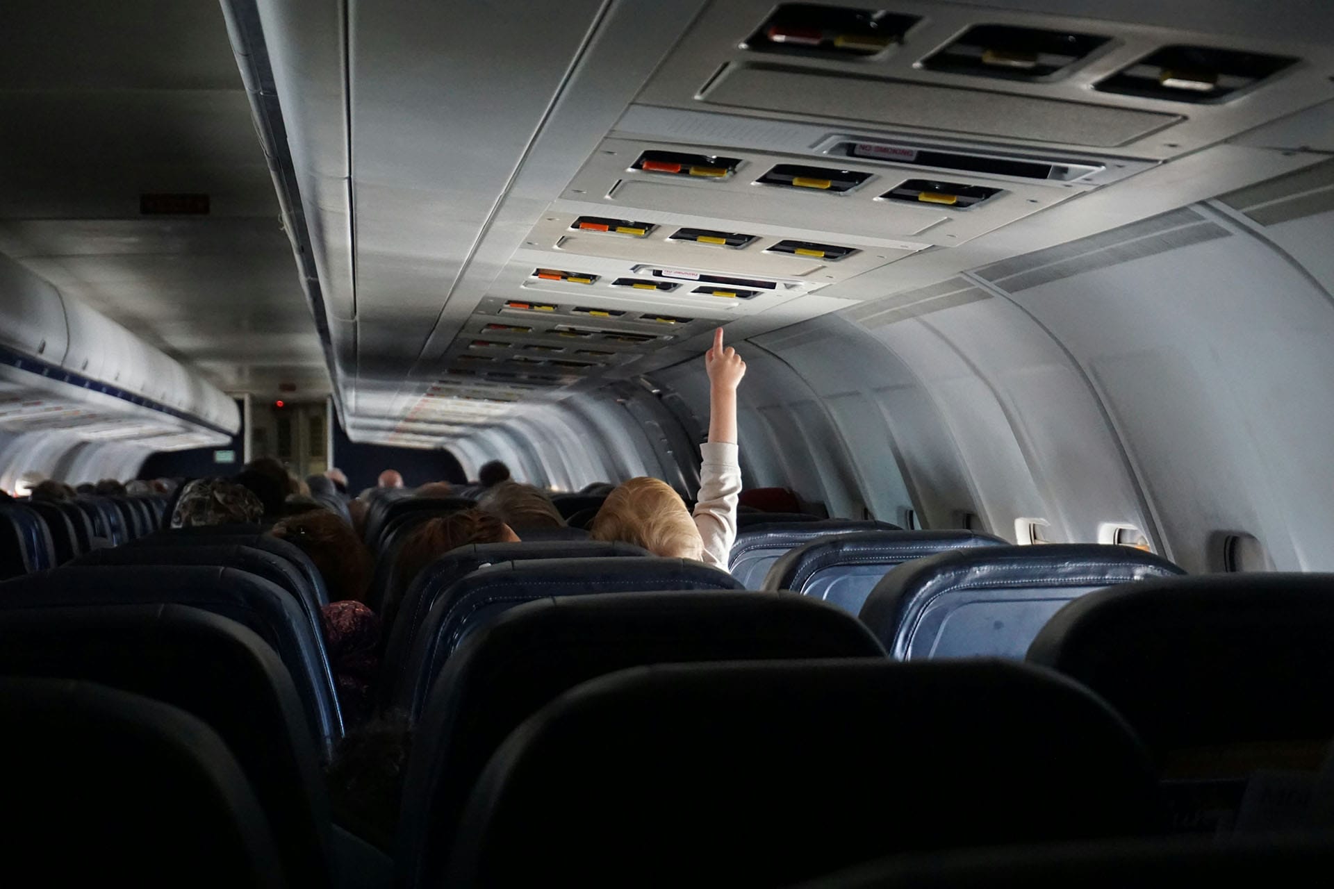 An image of the interior of an airliner in flight with a passenger reaching for the light switch