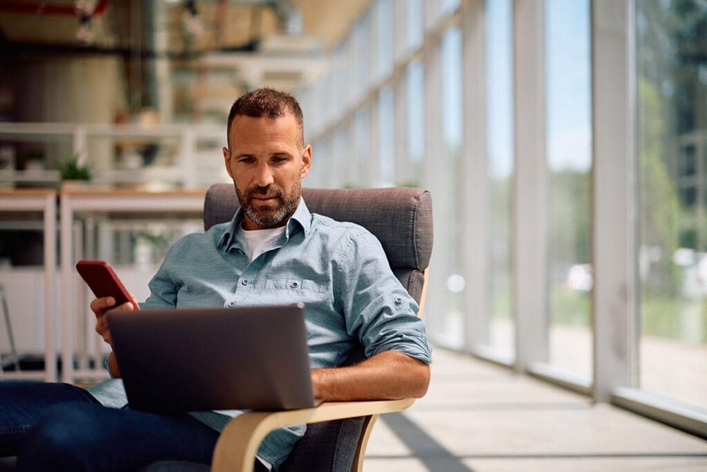 Een man in ontspannen kleding controleert zijn vluchtgegevens op een laptop in een lounge op het vliegveld